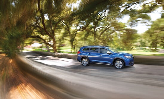 A blue Subaru Ascent driving between trees