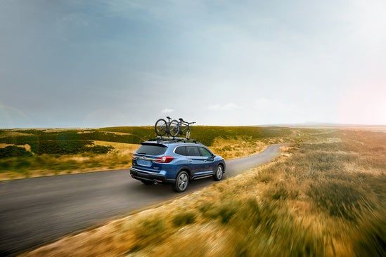 blue Subaru with bikes mounted on the roof driving on a rural road