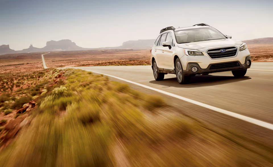 white Subaru Outback driving on a remote desert highway