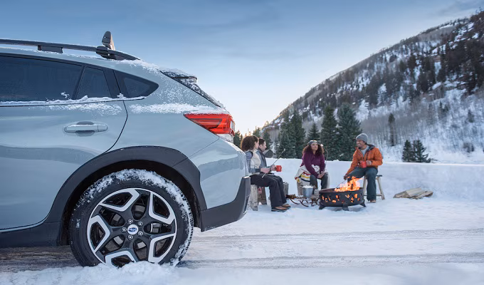 4 people sitting around a campfire next to their Subaru in the wintertime