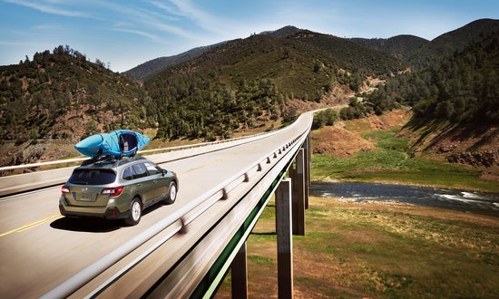 Subaru with kayaks on the roof driving on a bridge into the mountains