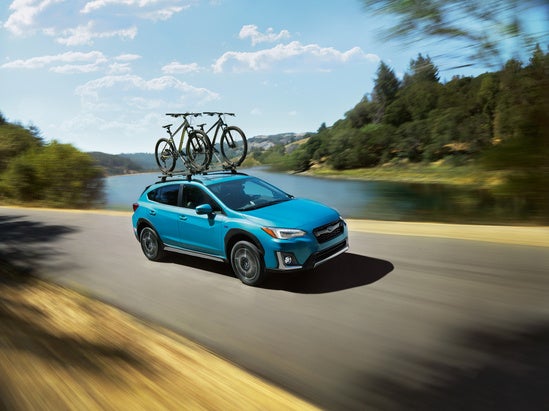blue Subaru Crosstrek with bikes mounted to the roof driving along a lakeshore