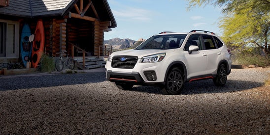 white Subaru Forester parked in front of a log home