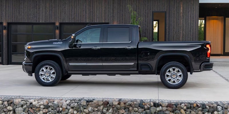 Side view of a dark grey or black Chevrolet High Country pickup truck parked in front of a modern dark building.