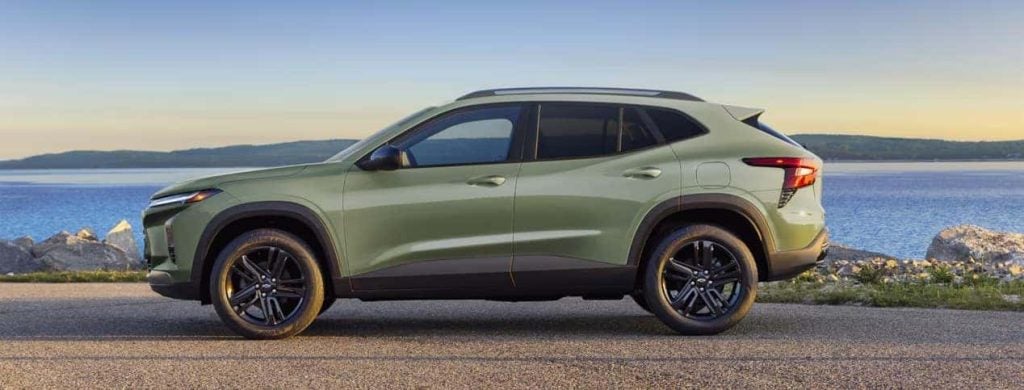 Side view of a light green SUV with black wheels parked near a lake with mountains in the background.