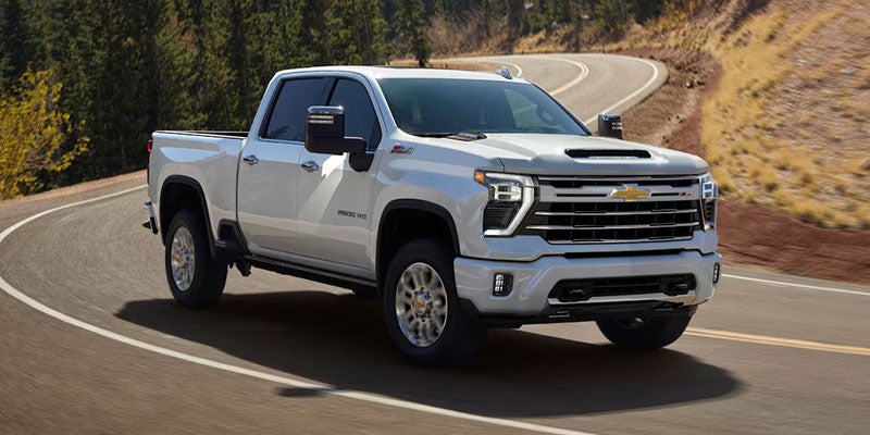 A white Chevrolet Silverado pickup truck drives around a curve on a mountain road 