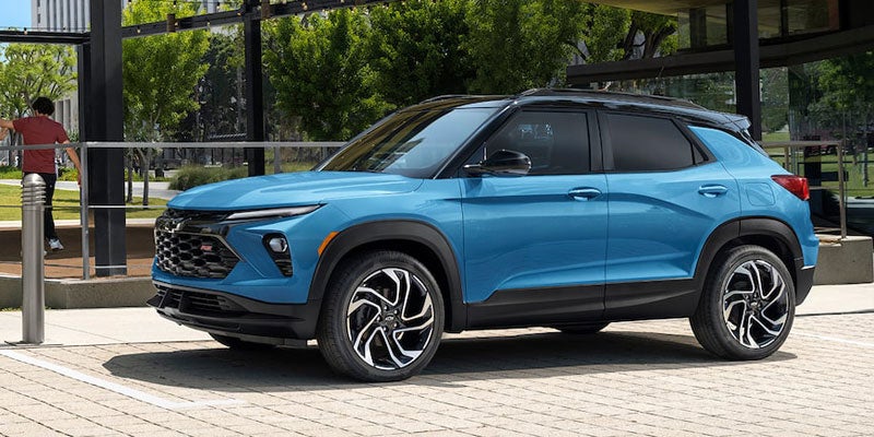 A bright blue Chevrolet Trailblazer parked left of center, with a person standing behind a barrier in the background.