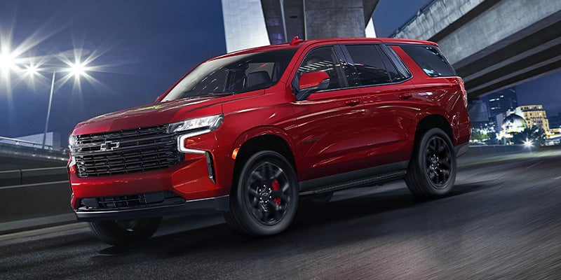 Shiny red Chevy Tahoe with dark wheels driving at night on a highway under an overpass.