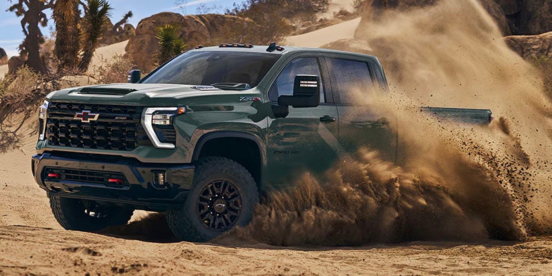 Dark green heavy-duty pickup truck driving aggressively through sandy desert terrain