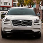 Front view of a sleek, white SUV parked on a city street. The vehicle has a modern design with a distinctive grille. Background shows buildings and trees.