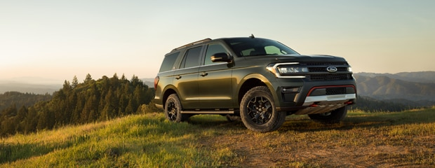 SUV parked on a grassy hilltop at sunset, against a backdrop of rolling hills and a clear sky. The scene conveys a sense of adventure and freedom.