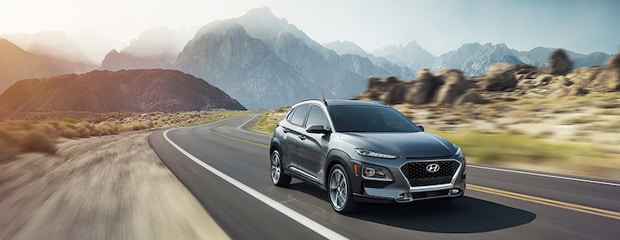 A sleek SUV drives on a winding road through a mountainous desert landscape under a clear sky, conveying adventure and freedom.