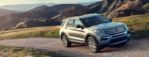 Silver SUV driving on a dirt road through rolling green hills under a clear blue sky, conveying a sense of adventure and freedom.
