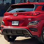 Red Hyundai SUV parked on pavement, showcasing the sleek design of its rear end with distinct taillights and dual exhaust pipes, conveying a sporty feel.