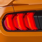 Close-up of an orange car's rear taillight, featuring a sleek, modern design with three vertical red light segments, conveying speed and style.