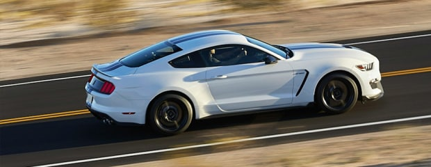 A white sports car speeds along a deserted highway, surrounded by desert landscape. The scene conveys a sense of freedom and adventure.