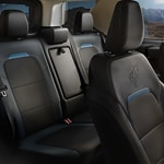 Interior of a modern car showcasing black leather seats with blue accents, featuring a sleek, spacious design. Sunlight filters through the windows.