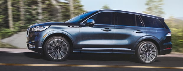 A sleek blue SUV speeds along a road with a blurred forest background, conveying motion and adventure. The vehicle's modern design is highlighted.