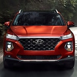 Front view of a shiny red SUV on a road, featuring a bold grille and sleek headlights, surrounded by blurred greenery, conveying power and elegance.
