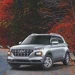 Silver SUV on a winding road lined with vibrant autumn foliage. The scene conveys a sense of adventure and tranquility in nature.