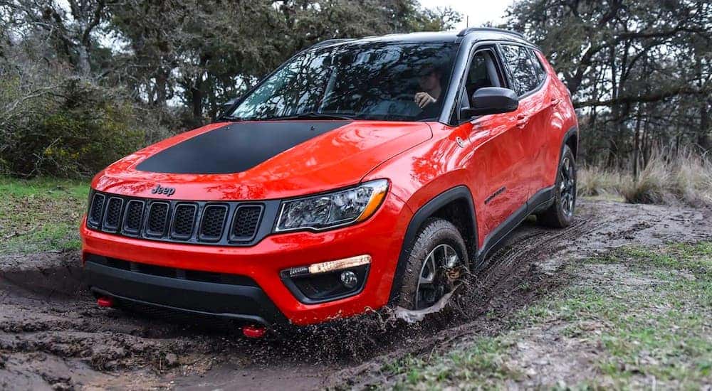 An orange 2019 used Jeep Compass is showing splashing through a mud puddle in the woods.