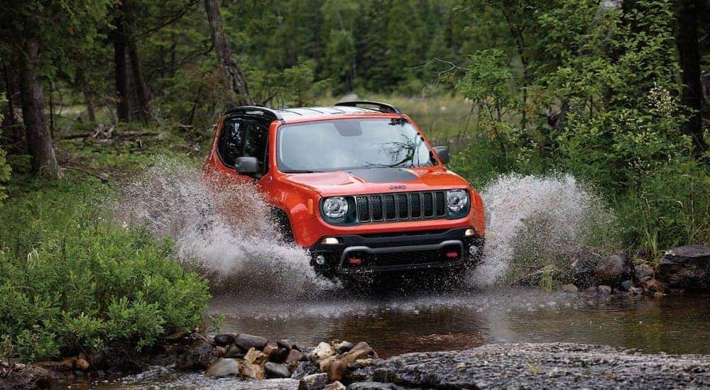 An orange 2020 Jeep Renegade Trailhawk from a Jeep dealer near you is driving through a river.
