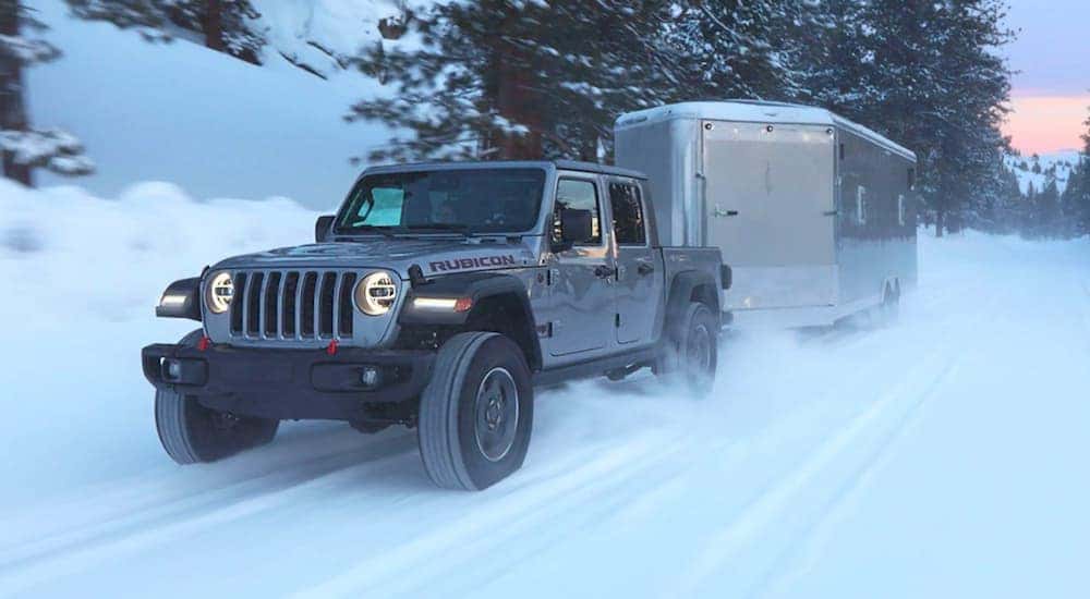 A gray 2020 used Jeep Gladiator Sport Rubicon is shown driving a trailer through the snow.