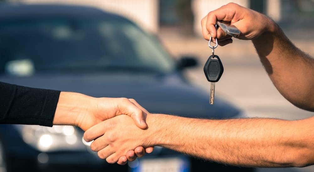 A salesman is shaking hands and passing a car key at a Lexington used car lot.