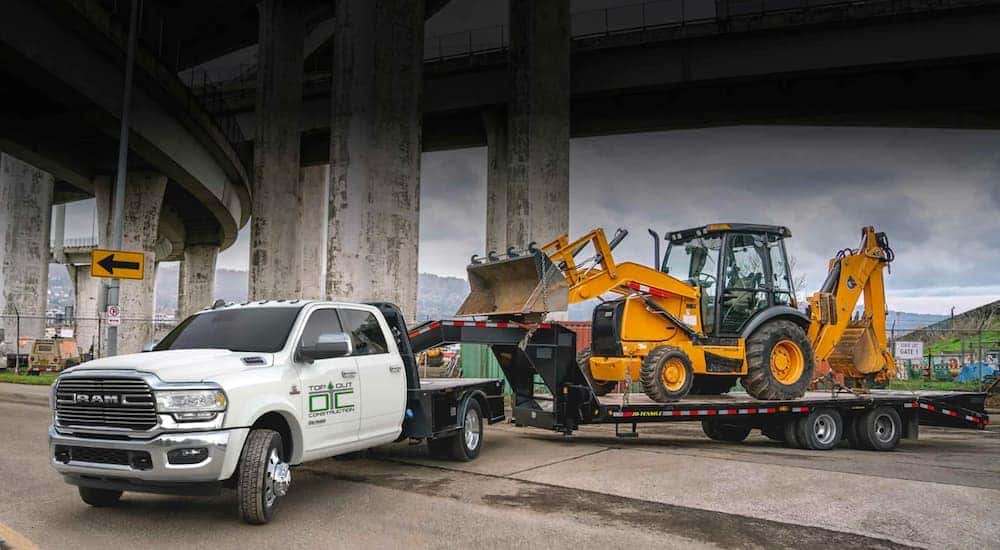 A popular Ram commercial vehicle, a white 2020 Ram Chassis Cab, is towing a backhoe on a gooseneck trailer.