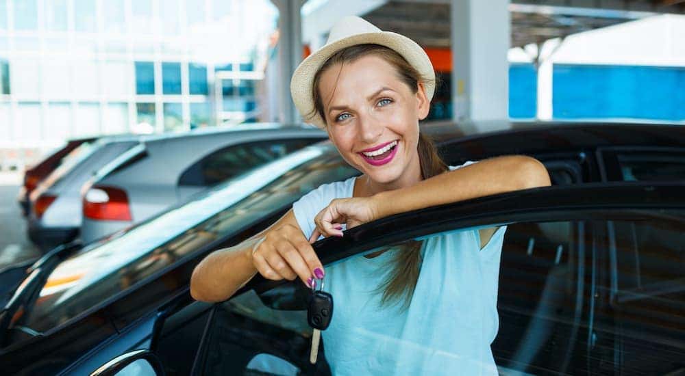 A woman is standing in front of an open car door at a Lexington used car lot.