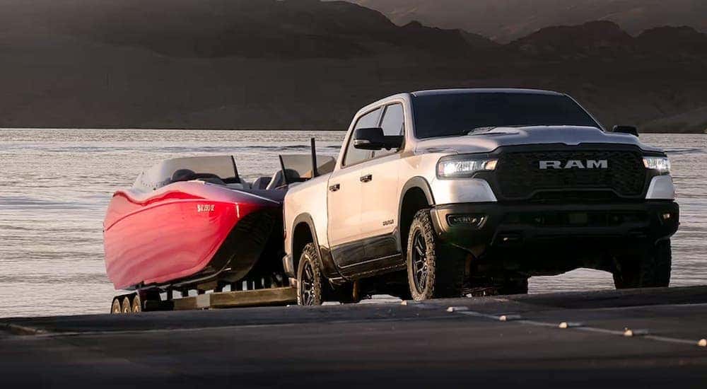 A silver 2025 Ram 1500 towing a red boat.