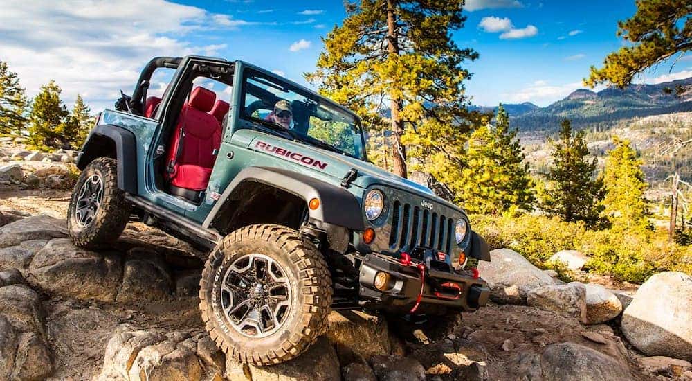 A blue 2009 used Jeep Wrangler Rubicon is shown crawling over a pile of rocks with no roof and doors.