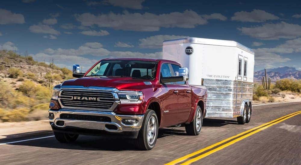 A red 2020 Ram 1500 is towing a trailer on a desert road.
