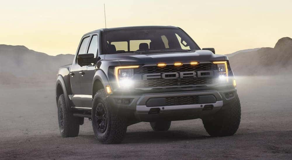 A grey 2021 Ford Raptor is driving through a field.