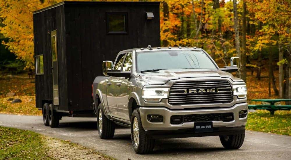 A silver 2019 Ram 2500, which is popular among used trucks for sale in Lexington, KY, is towing a black tiny house past fall foliage.