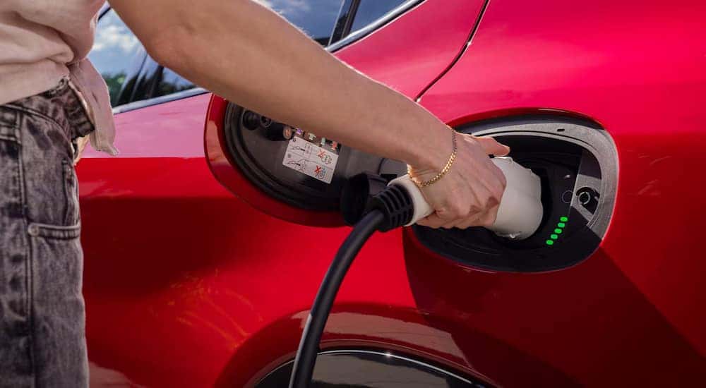 A close up of a person using the electric charging port on a red 2024 Dodge Hornet R/T is shown.