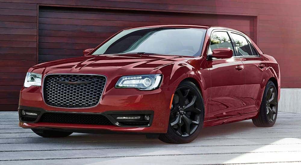 A red 2021 Chrysler 300 is shown parked in front of wooden garage.