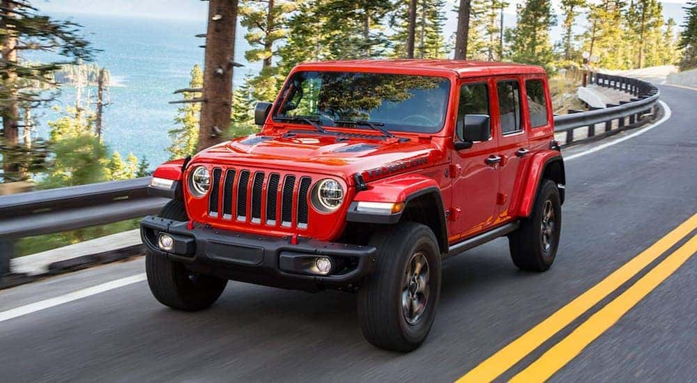 A red 2021 Jeep Wrangler Rubicon is shown driving on a highway to a used Jeep dealership.