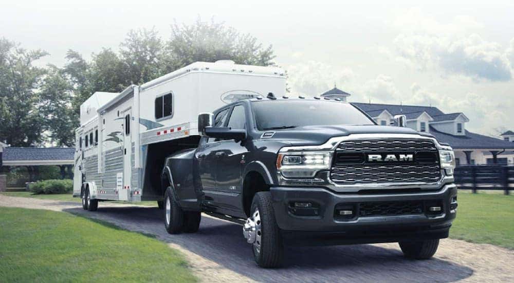 A black 2019 Ram 3500 is towing a white horse trailer away from a large home.