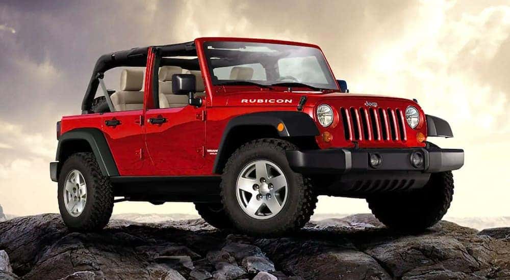 A red 2018 Jeep Wrangler Rubicon Unlimited is shown from the front, angled right, while parked on a rock pile.