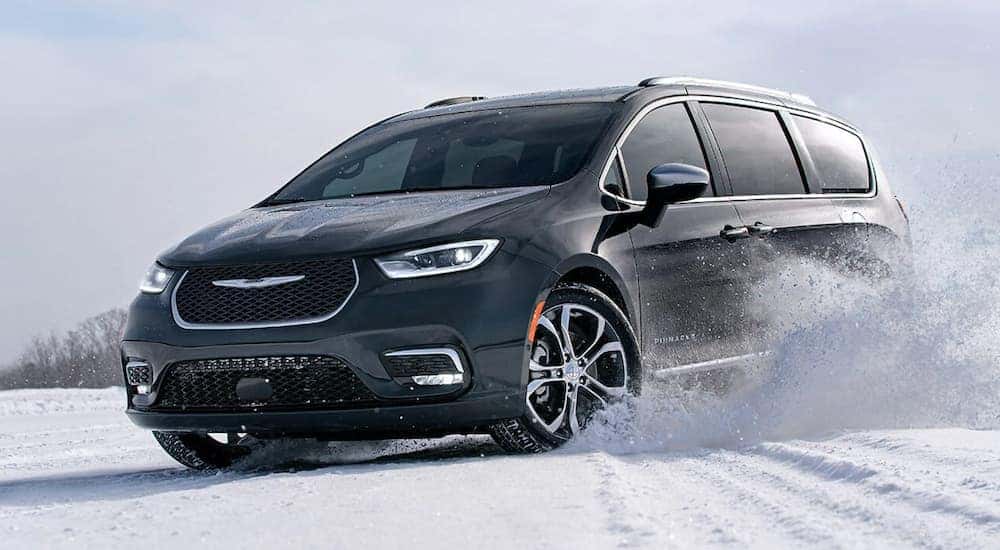 A black 2021 Chrysler Pacifica is shown driving through the snow after searching for new cars in stock near you.