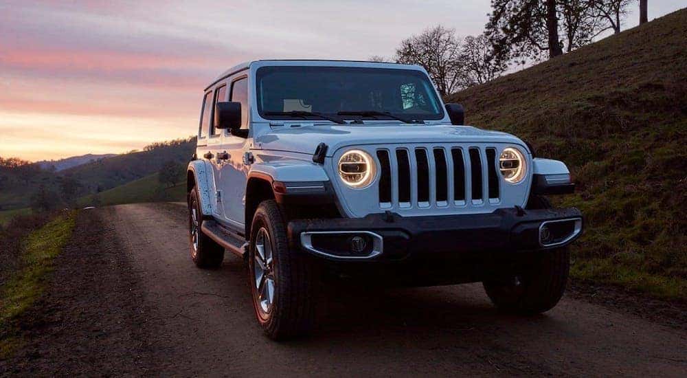 A white 2019 Jeep Wrangler Unlimited from a used car dealership near you is driving on a rural road at sunset.