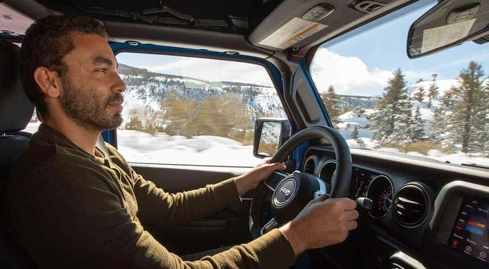 A man is shown from the passenger side driving a 2020 used Jeep Gladiator Sport Overland.