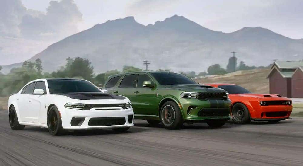 A white 2020 Dodge Charger, green Durango, and red Challenger are driving side by side past a mountain.