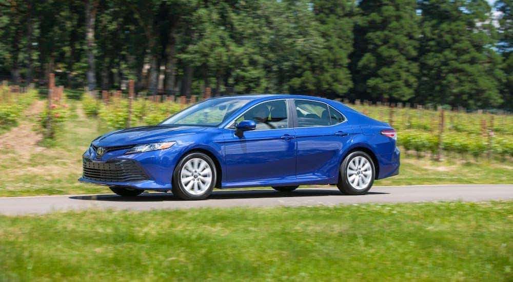 A blue 2017 Toyota Camry is driving on a rural road.