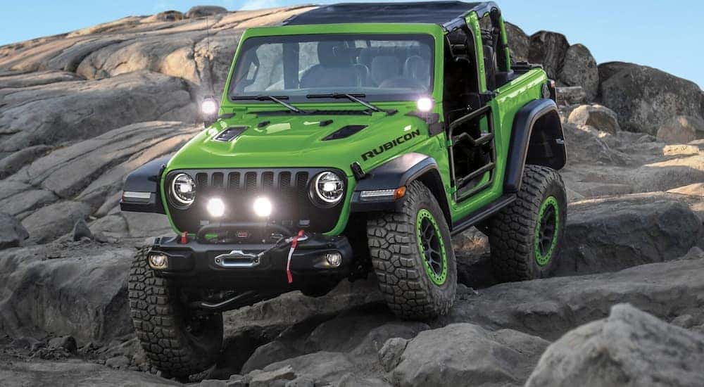 A popular used Jeep Wrangler for sale, a green 2018 Jeep Wrangler JL, is shown driving off-road.