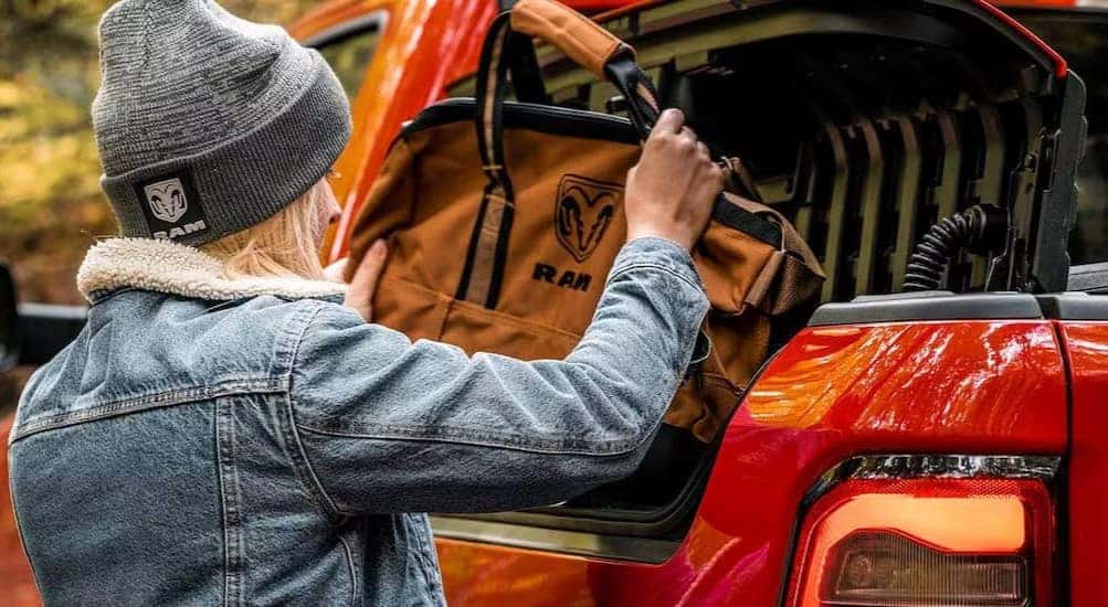 A person putting a bag in a cargo compartment on a red 2024 Ram 1500.