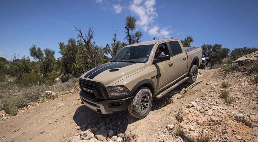 A tan and black 2017 used Ram 1500 is driving down a rocky hill.