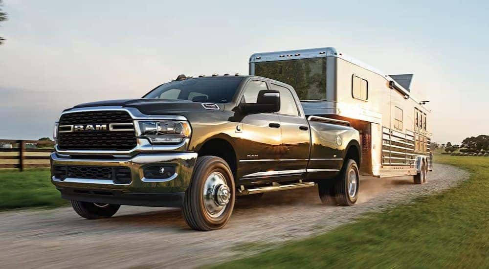 A black 2023 Ram 3500 is shown towing a horse trailer on a dirt road.