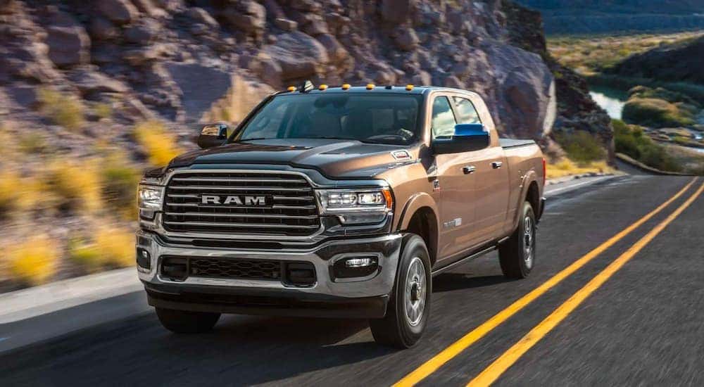 A brown 2020 Ram 2500 Laramie Longhorn is driving down the highway past a rocky wall.